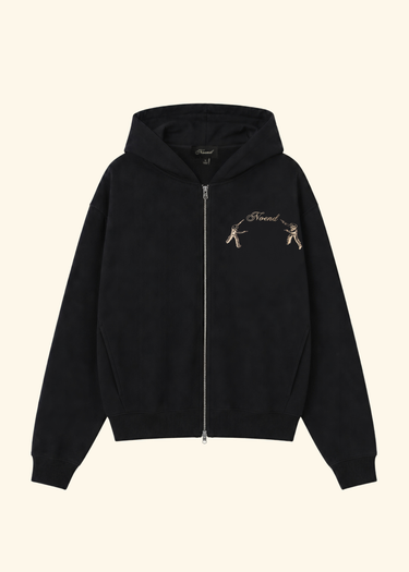 A black zip-up hoodie with a small embroidered graphic on the left chest depicting two figures and the text 'Friend', shown against a solid light beige background.