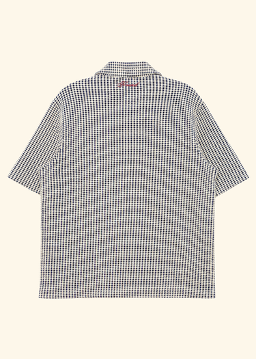 A short-sleeve button-up shirt with a small black and white micro-check pattern, shown from the back against a solid cream background.