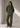 A woman stands in a minimalist studio wearing an olive green corduroy button-up jacket and matching wide-leg corduroy pants.