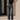 A woman wearing a black sleeveless top and dark gray high-waisted cropped jeans with rolled hems, standing outdoors against a concrete wall.