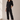 Woman wearing a black jumpsuit standing in a well-lit room with sunlight filtering through.