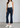 Woman wearing dark blue cropped flare jeans and white sneakers on a plain background