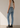 A woman shown from the back wearing light-wash blue skinny jeans, a light gray sleeveless top, and black ankle boots, standing against a plain beige wall.
