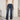 A model wearing dark blue cropped flare jeans, a white ribbed tank top, and black strappy flat sandals, standing in a bright, modern white interior setting.