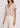 Woman wearing a beige V-neck top and light-colored pants against a white background