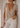 Woman wearing a beige v-neck t-shirt and white pants against a neutral wall.