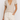 Person wearing a beige V-neck t-shirt and white pants on a plain background