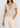 Person wearing a beige V-neck t-shirt and white pants on a plain background