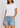 A woman wearing a white short-sleeve crewneck t-shirt and light-wash denim shorts, shown from the neck down against a light gray studio background.